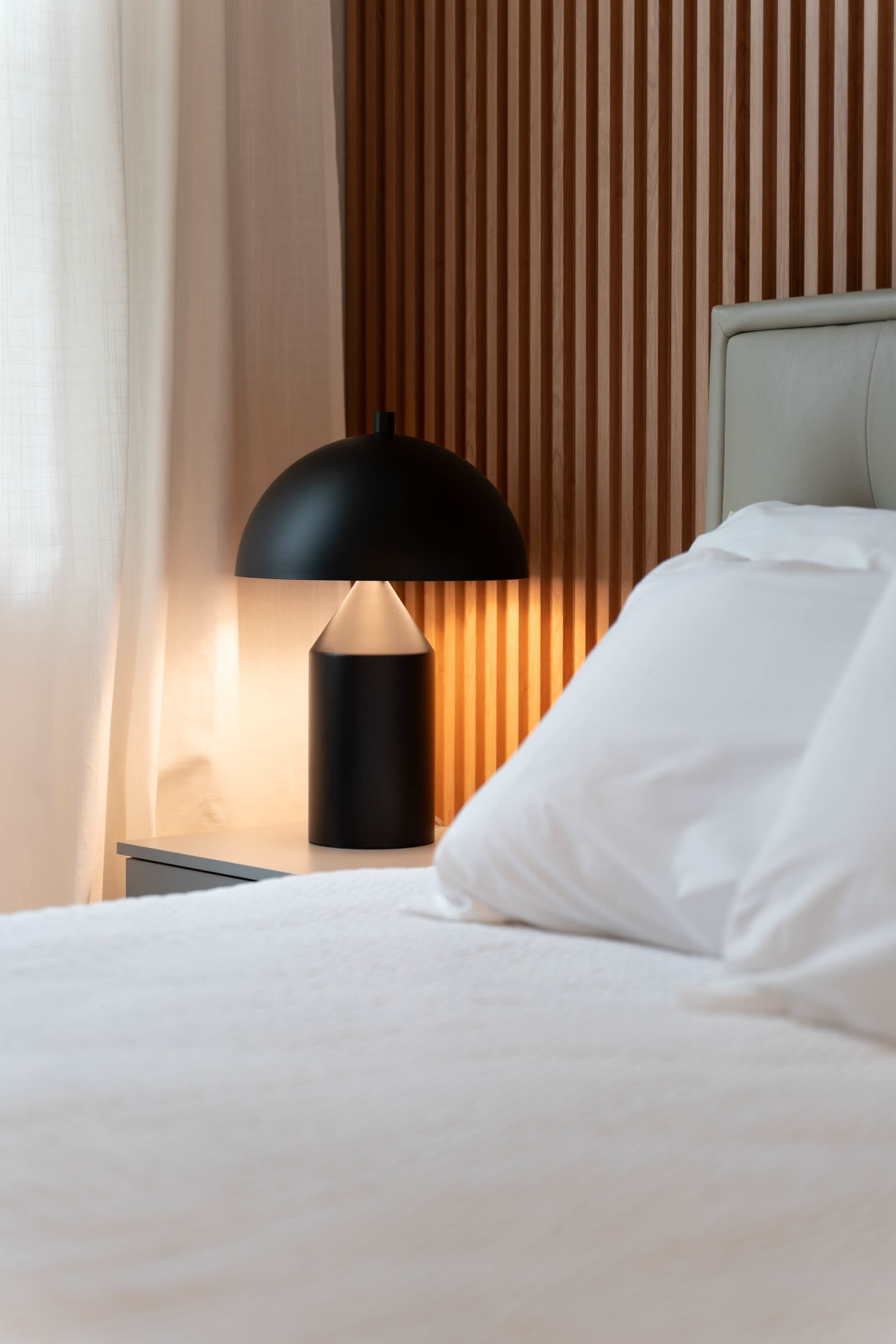 Minimal apartment bedroom with slatted wood headboard wall and dome table lamp